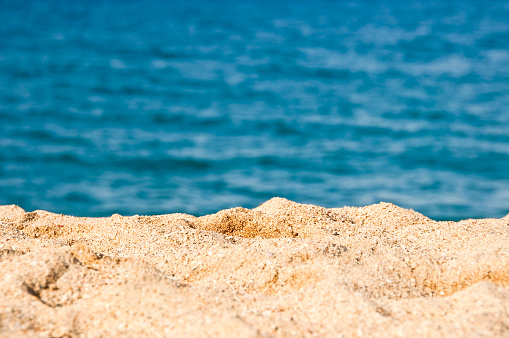 Close up on the sand of a beach, blue sea water in the background