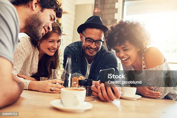 Friends Looking At Smart Phone While Sitting In Cafe Stock Photo - Download Image Now