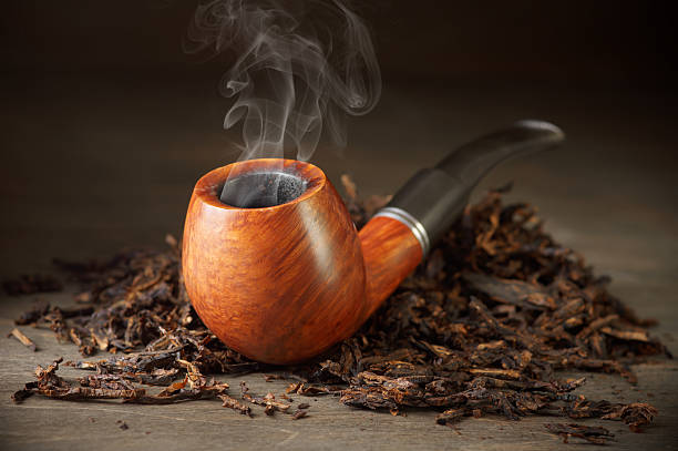 Pipe on tobacco pile Classic wooden pipe with smoke and tobacco pile on vintage wood. pipe smoking pipe stock pictures, royalty-free photos & images