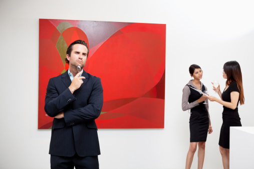 Young man thinking with two women talking in background in museum