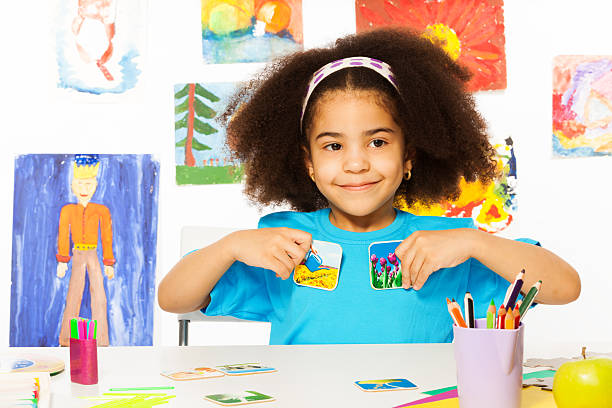 African girl plays developmental game, holds cards Cute African girl playing developmental game holding cards matching relation by table sitting in playroom with wall behind full of children drawings / !!! images on cards and other self made materials from my portfolio and property released as well as images on the wall autism photos stock pictures, royalty-free photos & images
