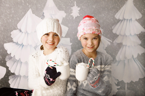 Identical twin sisters smile as they hold mugs of hot chocolate. They are ten years old.