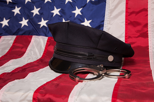 A police hat with handcuffs on an American flag background.