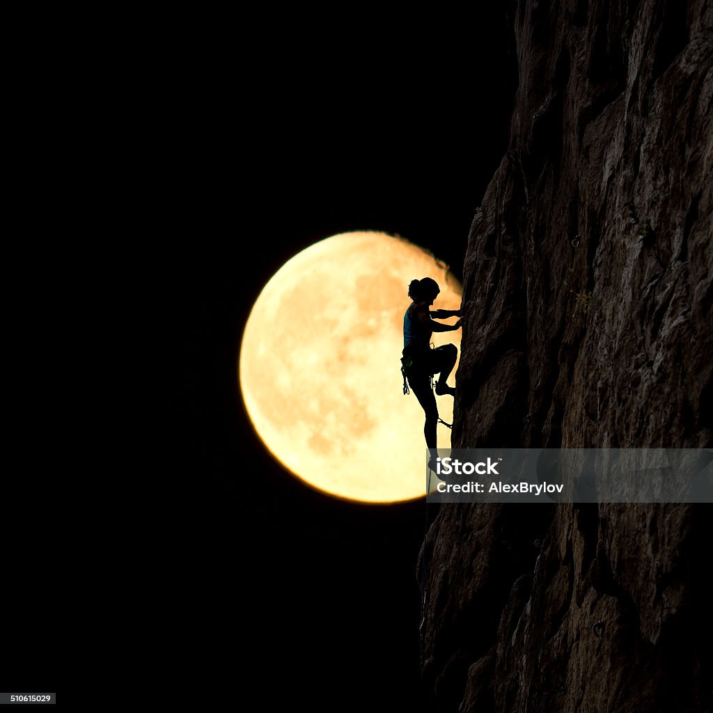 Moonlight climber Female rock climber ascends the natural rock at night with the large full moon on the background. Women Stock Photo