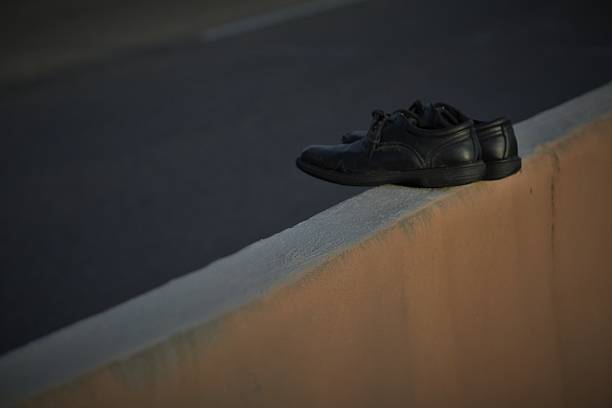 A pair of empty black shoes resting on a concrete barrier ledge next to a street.