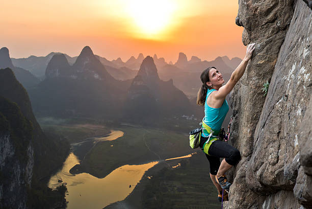Rock climbing in China Female extreme climber conquers steep rock against the sunset over the river. China, typical Chinese landscape with mountains and river rock climbing stock pictures, royalty-free photos & images