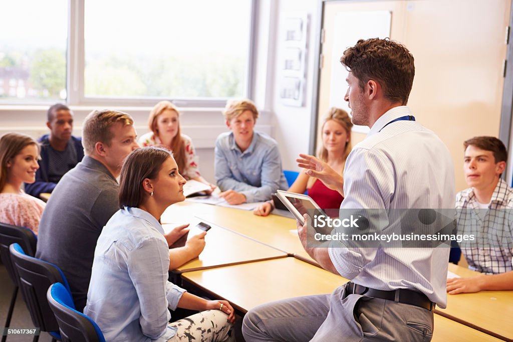 Teacher With College Students Giving Lesson In Classroom Teacher With College Students Giving Lesson In Classroom Holding A Digital Tablet Instructor Stock Photo