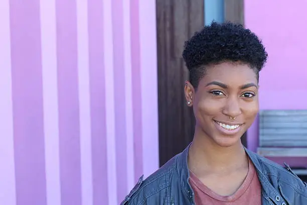 Pretty short hair girl with gray jacket posing against a fancy pink wall.