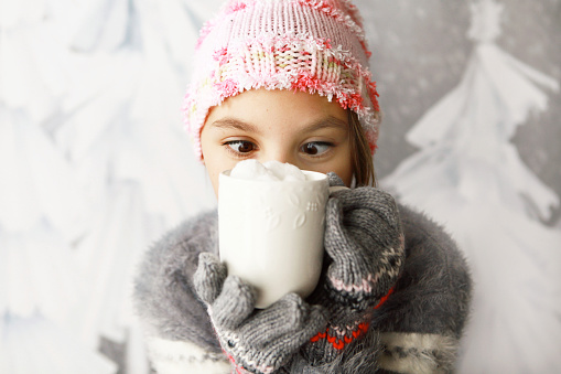 A ten year old girl looks with crossed eyes into her mug of hot chocolate. 
