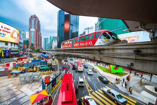 Kuala Lumpur, Malaysia - April 10, 2015: Downtown Kuala Lumpur crossing with road, train and billboards. Cars and a monorail car rush through the Bukit Bintang intersection.