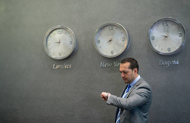 Business man checking the time on his watch with clocks hanging on the wall