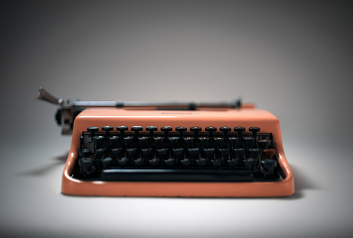 Vintage pink typewriter in evocative spotlight and focus. It could be the tool of a journalist, a writer or a secretary. Mood/concept of mystery, femininity and style