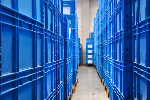 Piles of blue plastic containers in a warehouse in Germany. The boxes are used in the logistics chain transporting the produced goods.Selective focus on the front of the photo.
