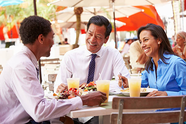 Three Businesspeople Having Meeting In Outdoor Restaurant Three Businesspeople Having Meeting In Outdoor Restaurant Smiling business lunch stock pictures, royalty-free photos & images