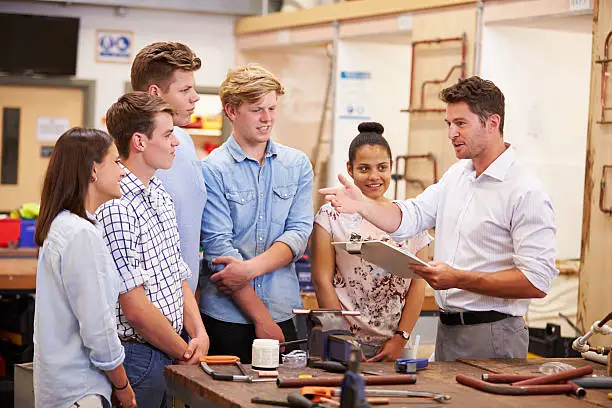 Teacher Helping College Students Studying Plumbing Holding A Clipboard