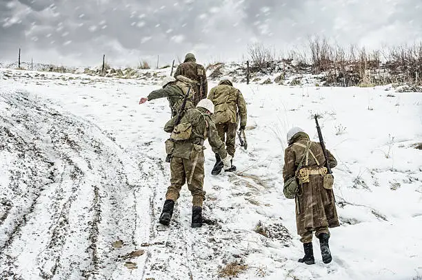 Five men from a WWII US MIlitary Squadron on Patrol In a winter Blizzard.  The road is muddy and the skies are full of bluster and snow.  They look cold and miserable.  Copy Space.