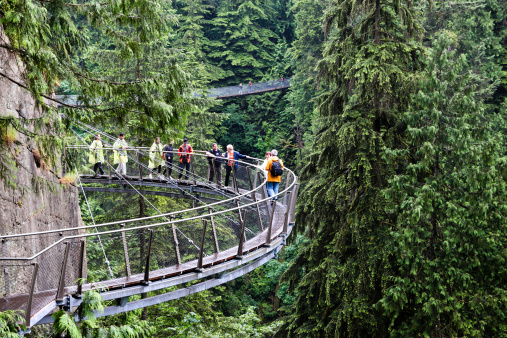 Vancouver, Сanada - June 29, 2011: Visitors explore the Capilano Cliff Walk through rainforest vegetation. The cantilevered and suspended walkways jut out from the granite cliff face 230 metres above the Capilano River.