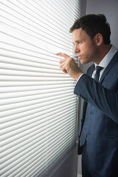 istock Unsmiling handsome businessman looking through roller blind 510658297