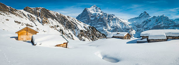 Snowy chalets in idyllic winter landscape under mountain peak panorama Traditional wooden chalets high in the Alps buried under crisp white snow below mountain peaks. ProPhoto RGB profile for maximum color fidelity and gamut. Grindlewald stock pictures, royalty-free photos & images