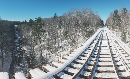 A panoramic view from the center of a snow covered abandoned railroad bridge spanning a steep river valley.  Stitched images.