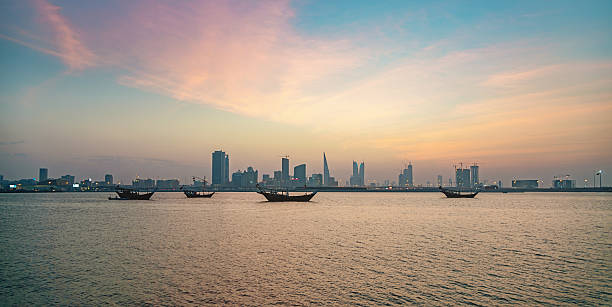 Bahrain Manama City by Night Manama Skyline Panorama - typical bahrain boats anchored in the sea, office buildings, hotels and the world trade center of bahrain at twilight under beautiful skyscape. Manama, Bahrain, Middle East. manama stock pictures, royalty-free photos & images