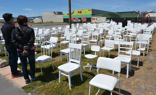 Christchurch, New Zealand - December 4, 2015: Visitors at 185 empty white chairs Sculpture. The artwork reflect the loss of lives, each chair represent one of the 185 lives lost in the 2011 Christchurch earthquake.