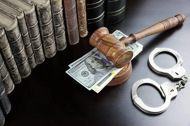 Judges Gavel, Handcuffs, Dollar Cash And Old Law Book  On The Black Wooden Table Background In The Back Light. Overhead View.