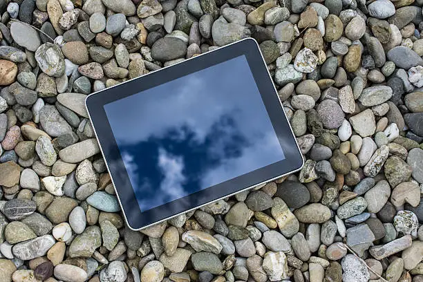 Reflection of the cloudscape on the ground on  a digital tablet  lying on the gravelpath