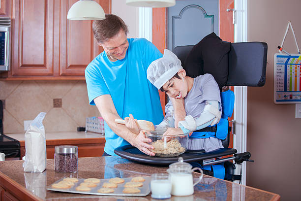 Father helping disabled son bake cookies in kitchen stock photo