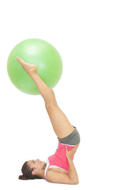 Content sporty brunette holding exercise ball between legs on white background