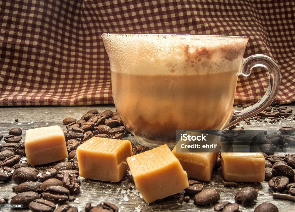 Salted Caramel Latte With Caramel, Coffee Beans And Sea Salt Salted caramel latte surrounded by coffee beans, caramels, and sea salt. Shot from a side view with selective focus and a rustic gingham background. Caramel Stock Photo