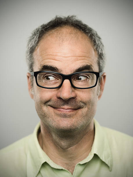 Portrait of a happy caucasian real man Portrait of a real caucasian man with suspicious expression. Short grey hair, glasses and brown eyes. Around 45 years old british. Vertical color image from a DSRL camera in studio. smirk stock pictures, royalty-free photos & images