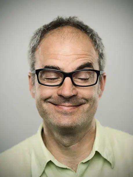 Portrait of a real caucasian man with playful expression. Short grey hair, glasses and brown eyes. Around 45 years old british. Vertical color image from a DSRL camera in studio.