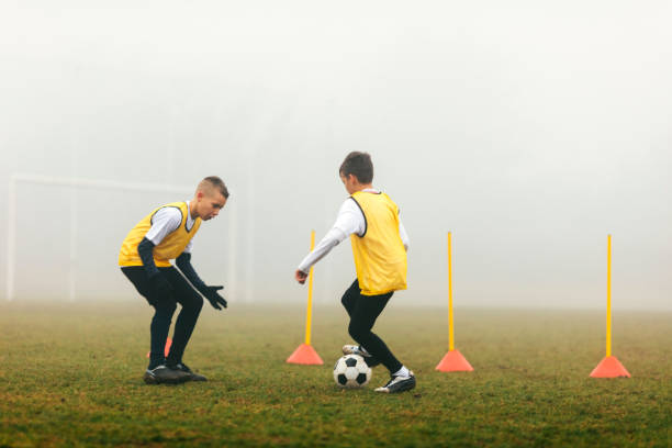 Elementary age soccer athlete kicks ball around cones.