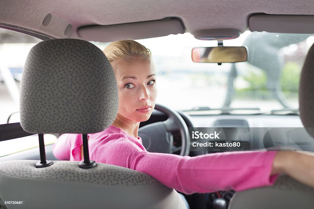 Lady looking back while reversing. Beautiful young lady looking back through the rear window from the front seat of a car while reversing. Car Stock Photo