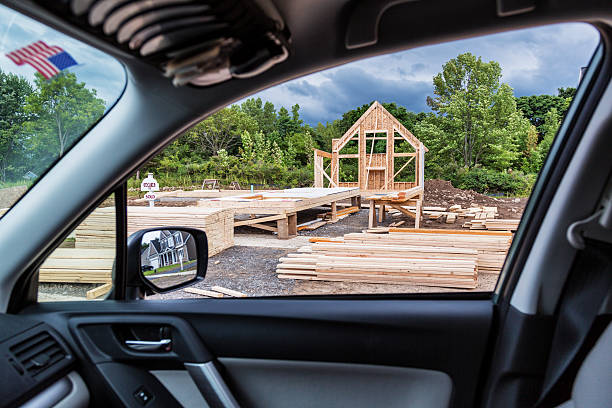 New Home Construction Through Car Window A view of a residential development construction site - with a new house just beginning to be framed - through the passenger side window of a car. The home a few doors away reflected in the car's mirror is almost complete and ready for sale. sawhorse stock pictures, royalty-free photos & images