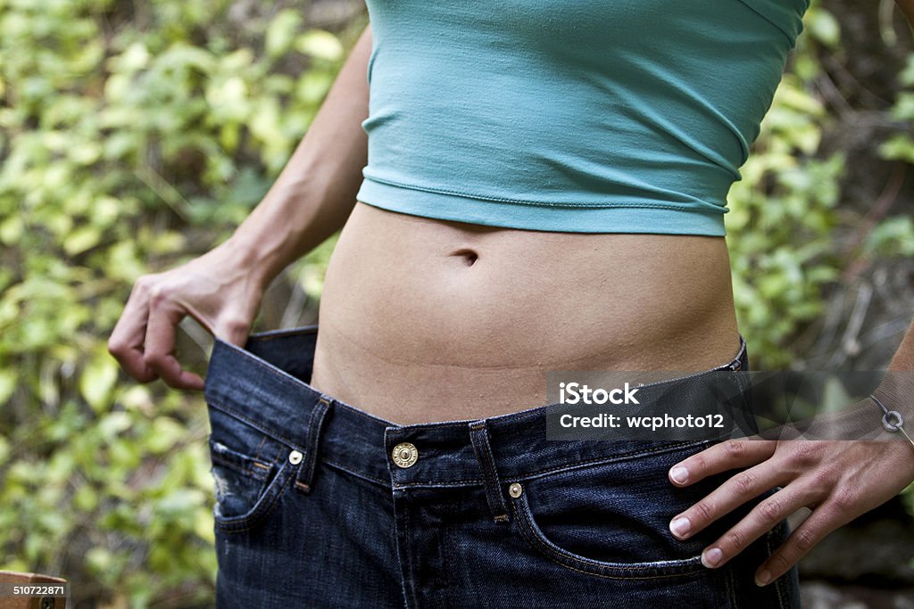 Losing weight around waist in blue jeans Losing weight around waist in blue jeans. Female wearing tanktop with abs showing Abdomen Stock Photo