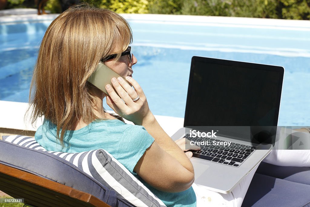 Modern business woman working on holiday Modern business woman sitting at garden with phone and laptop at home. Small business. Swimming Pool Stock Photo