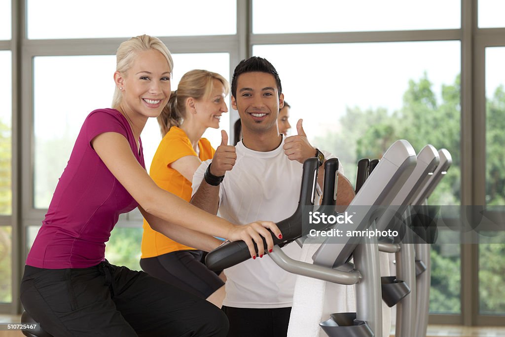 fully motivated fitness training young fitness trainer showing both thumbs up with woman on ergo bike Adult Stock Photo