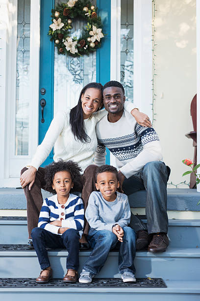 African American family with two children sitting on front steps African American family with two children (twins, 5 years) sitting outside house on front steps.  Christmas wreath hanging on front door. front stoop photos stock pictures, royalty-free photos & images