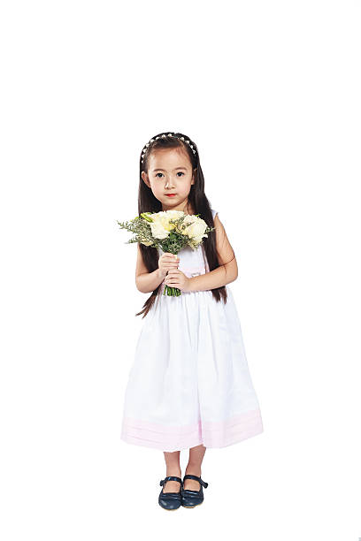 Portrait of a young girl in a white dress holding a daisy close to the camera, with a soft focus green background