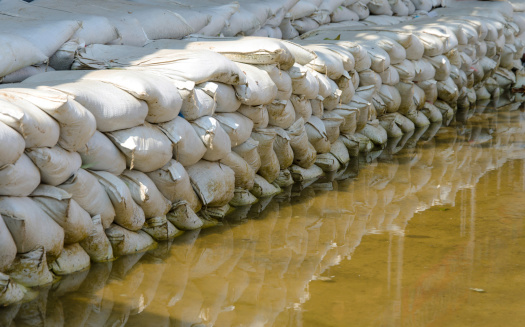 White sandbags for flood defense and it's reflection brown water.