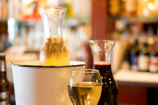 Carafes filled with red and white wine on a bar.  The white carafe sits in an ice bucket.   rm