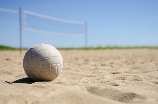 A multi-colored beach volleyball in mid-air after hitting just inside red baseline tape on a sand court.