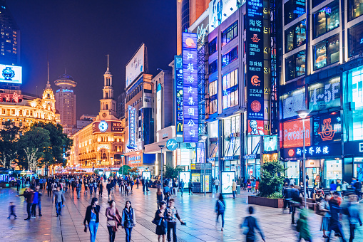 Crowds walk below neon signs on Nanjing Road. The street is the main shopping district of the city and one of the world's busiest shopping districts. 