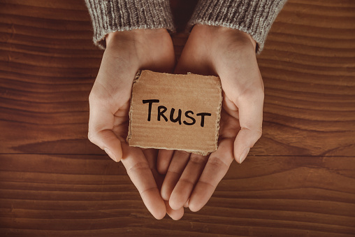 Hands holding piece of paper with word Trust