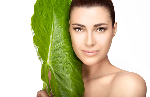 Beauty and skincare portrait. Beautiful spa girl with the large fresh green leaf of a tropical plant against her cheek as she looks at the camera with a gentle smile in a spa and wellness concept