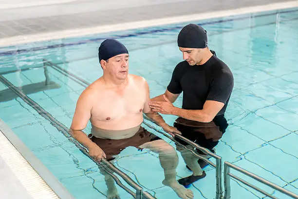 Man in physical therapy in the water with a physiotherapist - healthcare and medicine concepts
