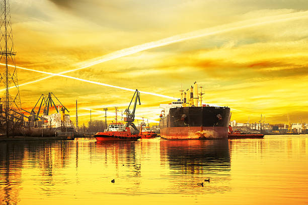 Big ship with escorting tugs leaving port at sunset.