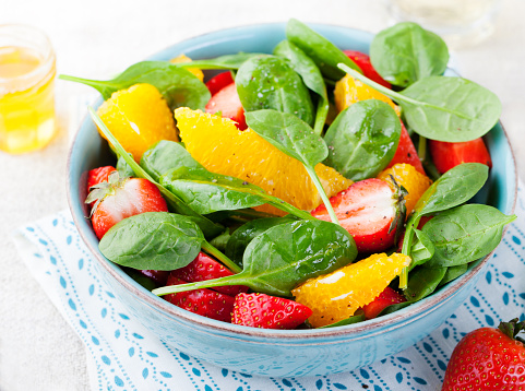 Fresh salad with strawberry, orange and spinach in a bowl on wooden background. Copy space